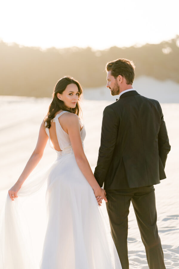 Bride and groom celebrate at the sand dunes at Moreton Island captured by Ben & Hope, relaxed Gold Coast wedding photographers.”