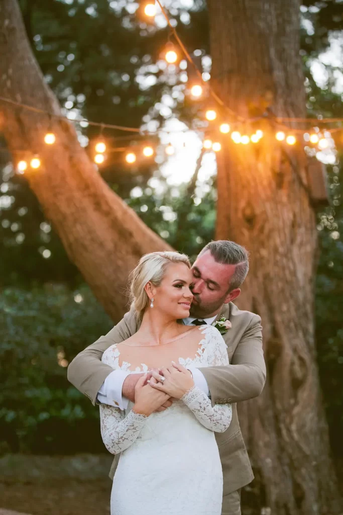 Bride and groom embracing under the trees lined with fairy festoon lights at gabbinbar homestead.