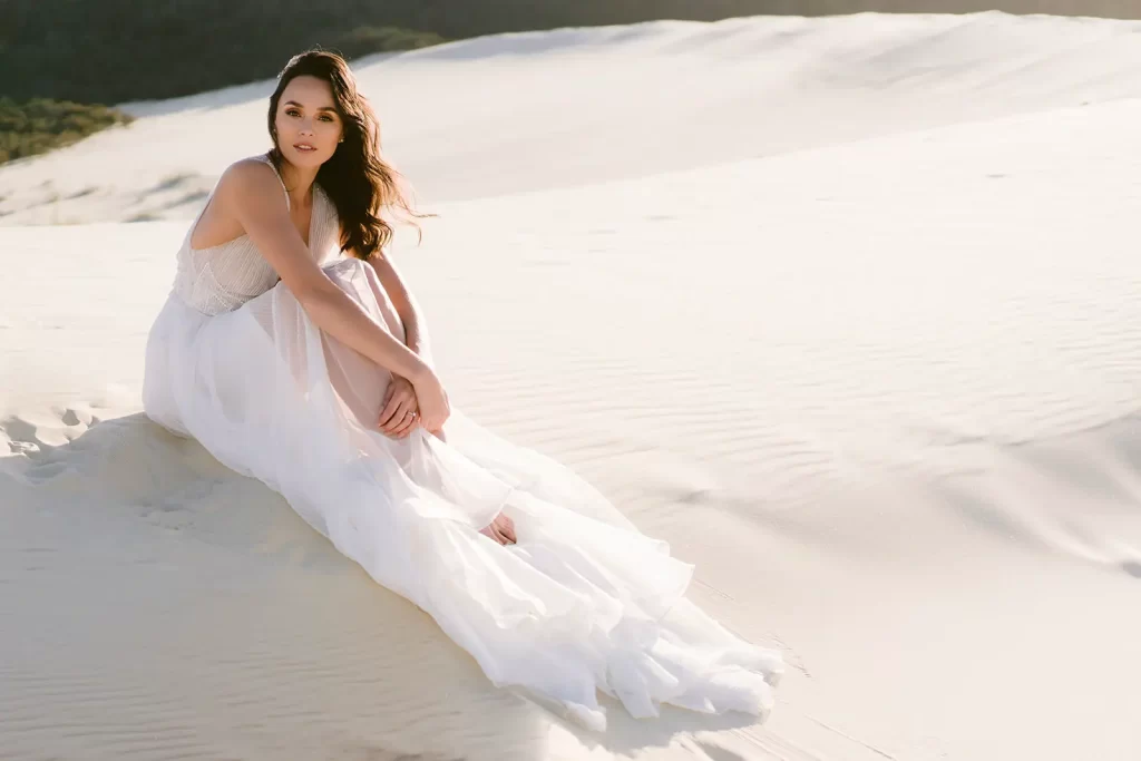 Bride sitting in the sand dunes on her wedding day